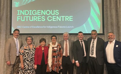 A group of men and women stand side by side on stage with a slide behind them reading Indigenous Futures Centre.